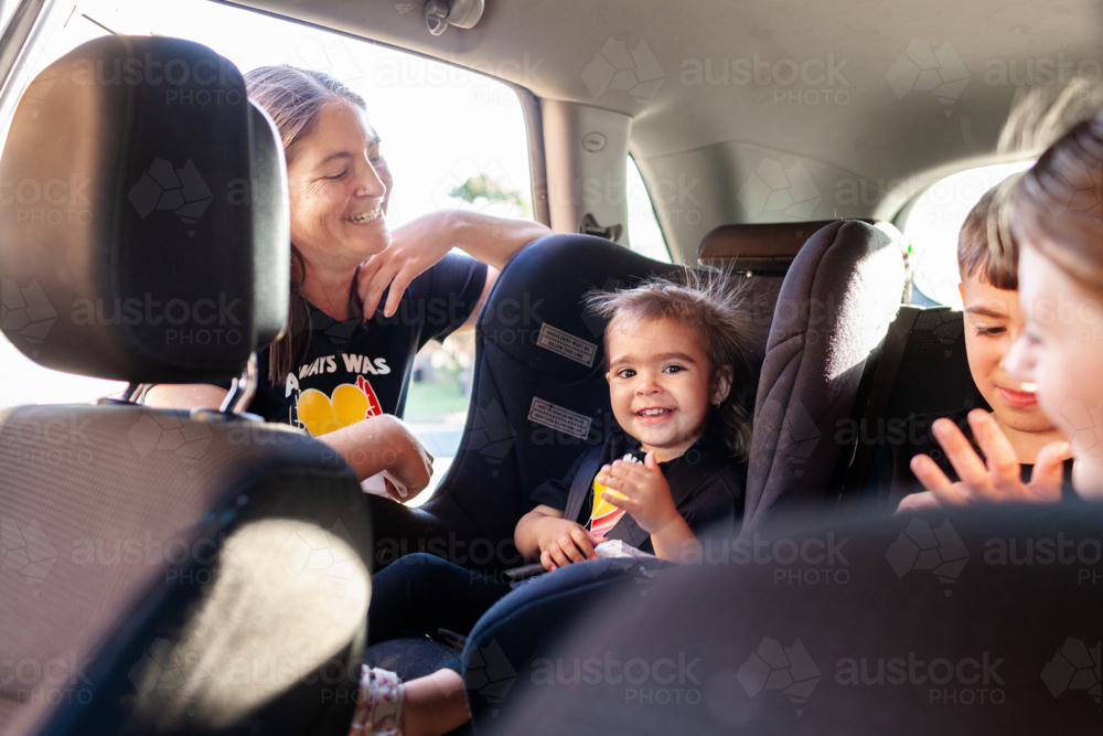 Australian mum putting Aboriginal toddler girl into forward facing car seat ready to travel - Australian Stock Image