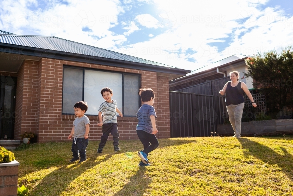 Australian mum running around with young boys in front yard of suburban home - Australian Stock Image