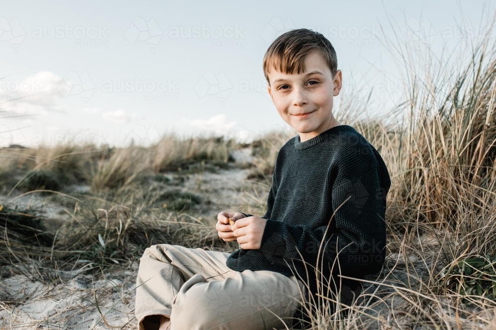 Autistic Boy sitting on a sand dune in the grass - Australian Stock Image