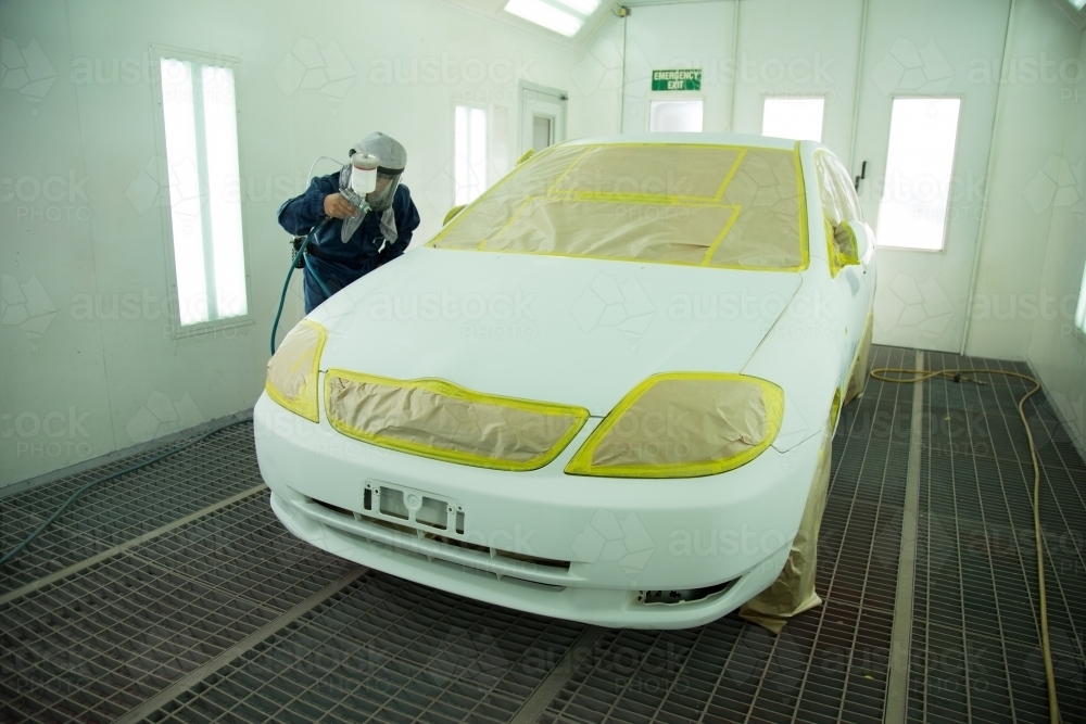 Auto painter in protective suit and mask, spraying a car in painting booth - Australian Stock Image