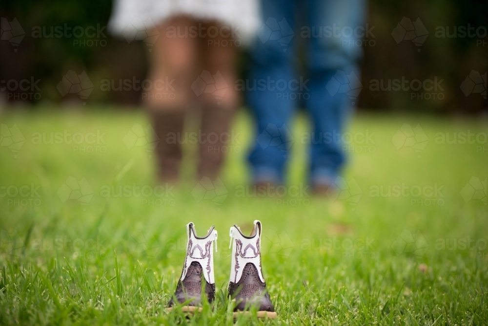 Baby boots with parents in blurred background - Australian Stock Image