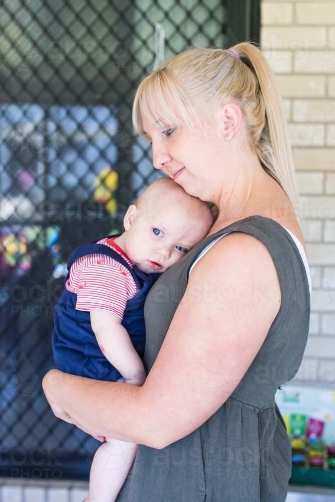 Baby boy cuddling into his mother while she holds him - Australian Stock Image