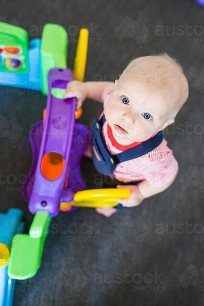 Baby boy looking up playing with colourful toy - Australian Stock Image