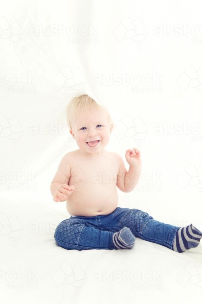 Baby boy under the covers smiling at camera - Australian Stock Image