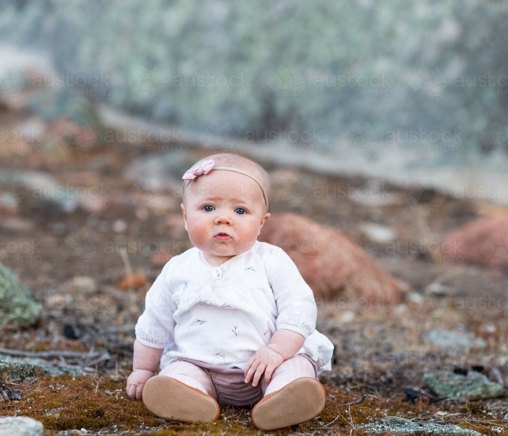 Baby girl sitting on ground with moss - Australian Stock Image