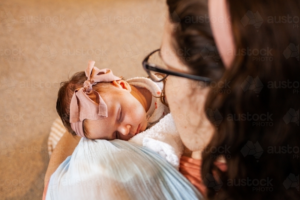 Baby girl wearing headband sleeping in mothers loving arms - Australian Stock Image