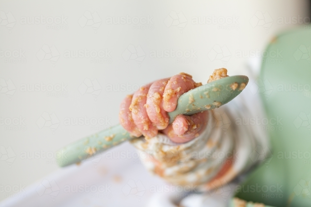 Baby hand covered in food holding spoon with copy space - Australian Stock Image