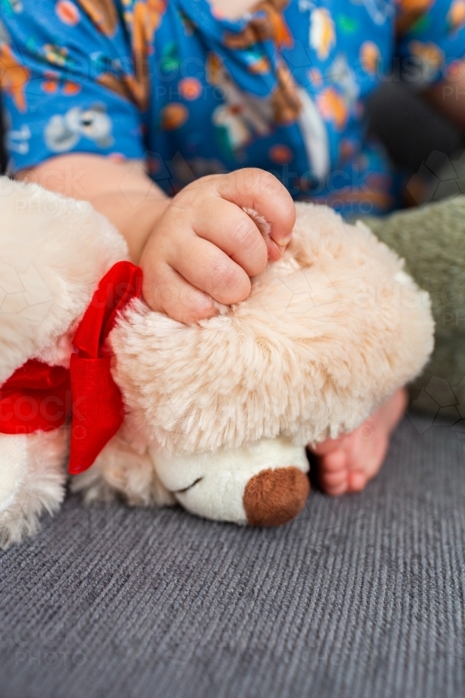 Baby hand holding onto plush toy teddy bear ear - Australian Stock Image