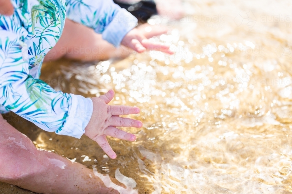 Baby hands splash excitedly in sparkling ocean water - Australian Stock Image