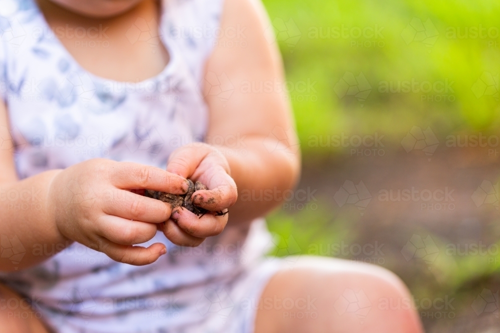 Baby holding small rocks in dirty hands outside - Australian Stock Image