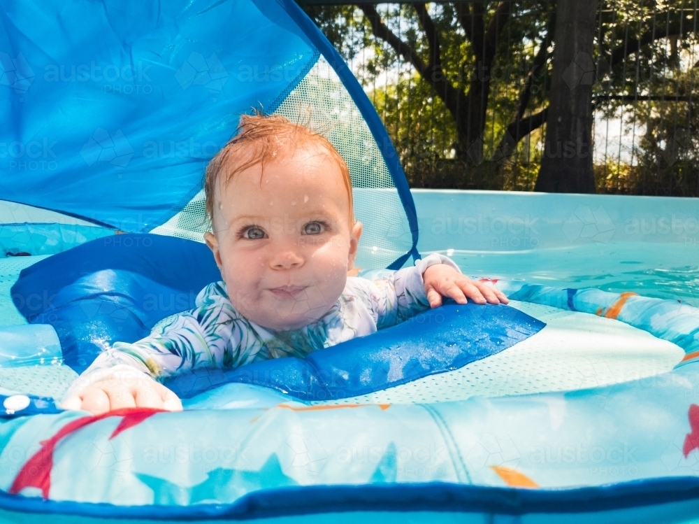 Baby in flotation device in backyard swimming pool in summer - Australian Stock Image