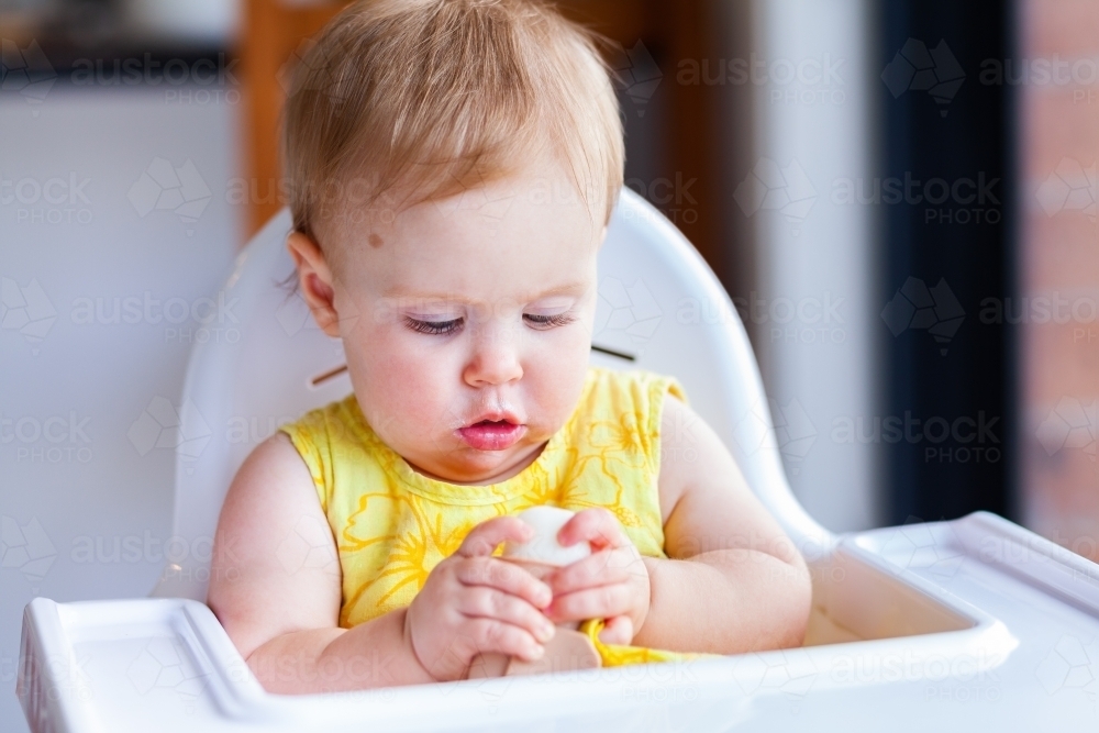 baby in high chair eating milk ice-block during hot summers day - Australian Stock Image