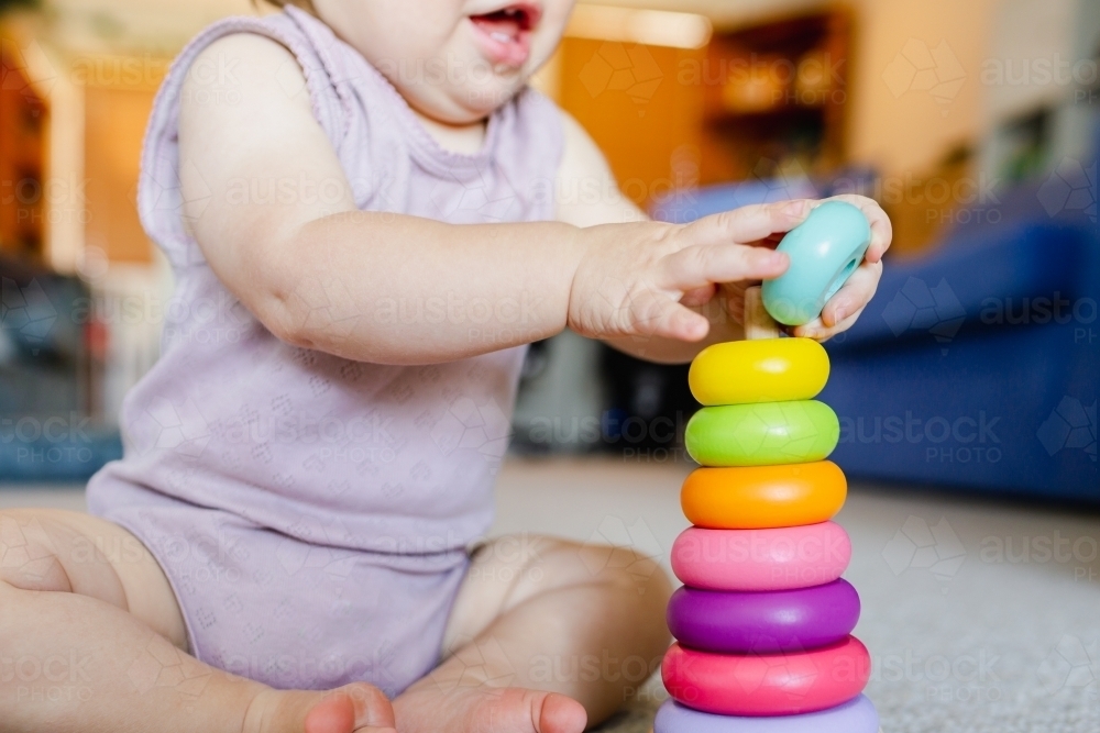Baby learning through play developing fine motor skills with colourful stacking toy - Australian Stock Image