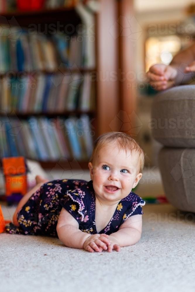 Baby on floor of library room with cheeky grin - Australian Stock Image