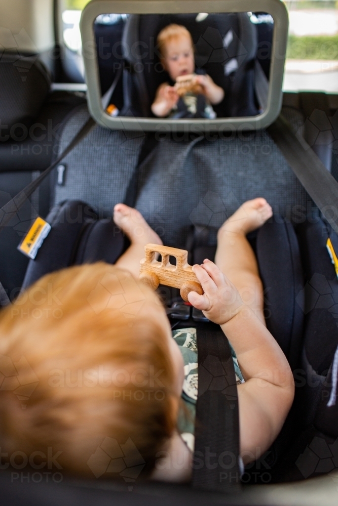 Baby playing in car with wooden toy car while travelling - Australian Stock Image