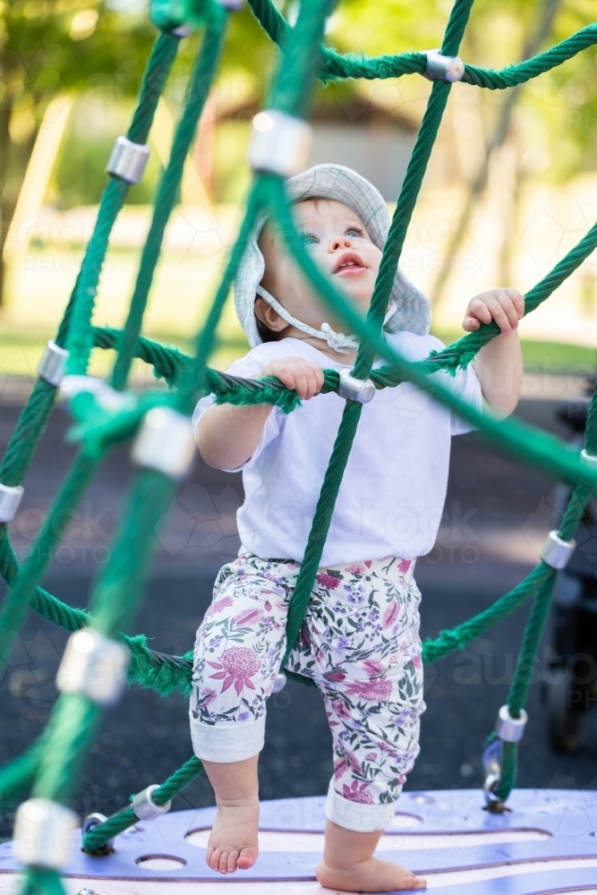 Baby playing on spinning climbing spiderweb frame at park - Australian Stock Image