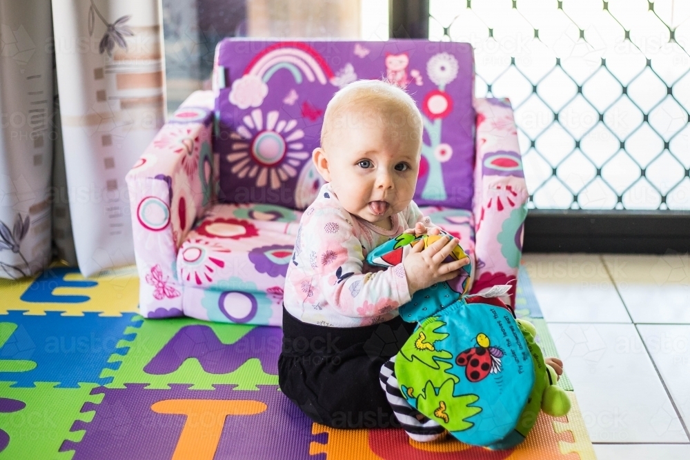 Baby poking tongue out playing with toy book - Australian Stock Image