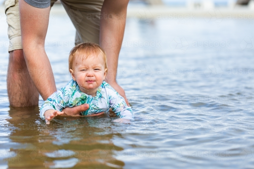 Baby pulling face after splashing water in ocean swimming pool - Australian Stock Image