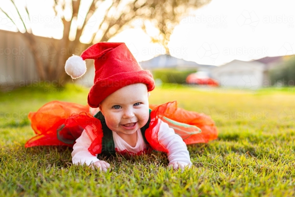 Baby ready for Christmas in red and greed outfit and Santa hat on grass - Australian Stock Image