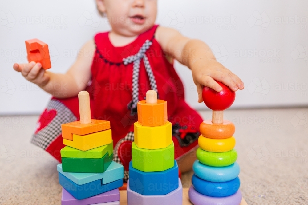 Baby sitting on floor playing with colourful stacking fine motor skills developmental toy - Australian Stock Image