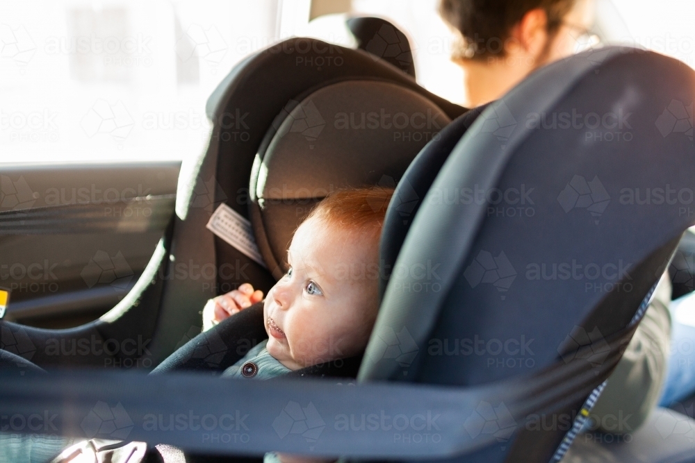 baby strapped into rear facing child car seat with parent in passenger seat in front - Australian Stock Image