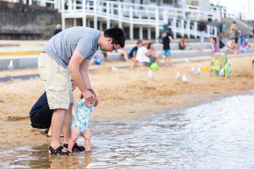 Baby walking into water at Merewether beach ocean baths on busy afternoon in summer - Australian Stock Image