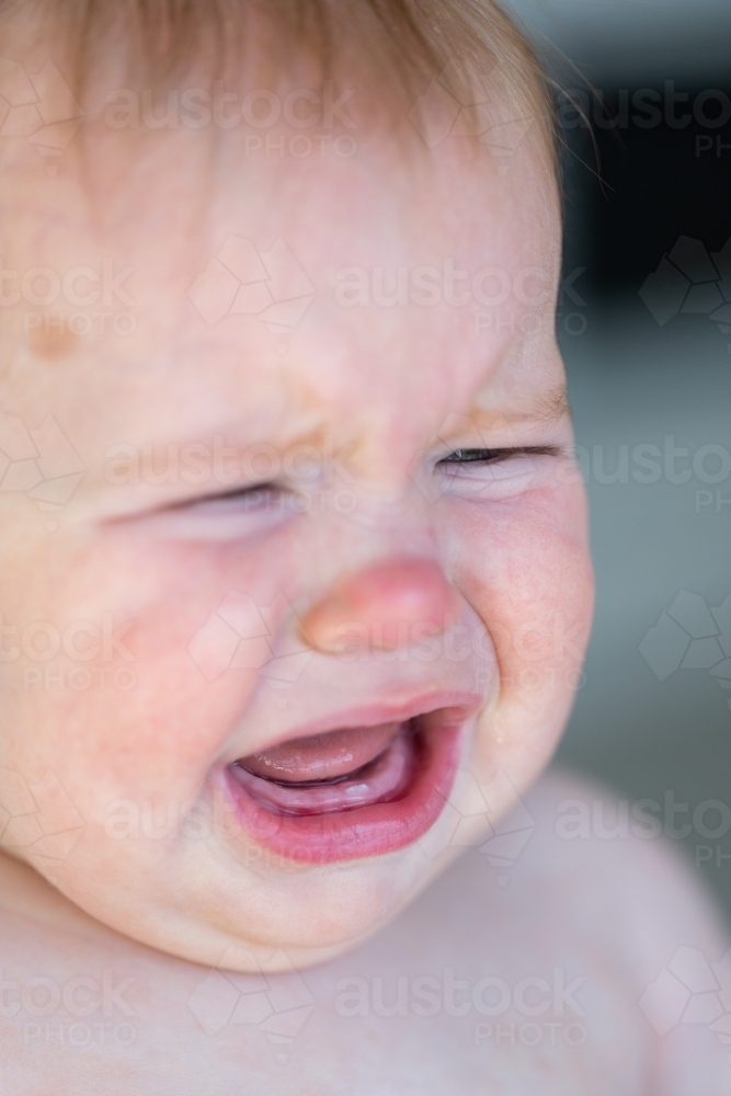 Baby with new first tooth looking sad crying - Australian Stock Image