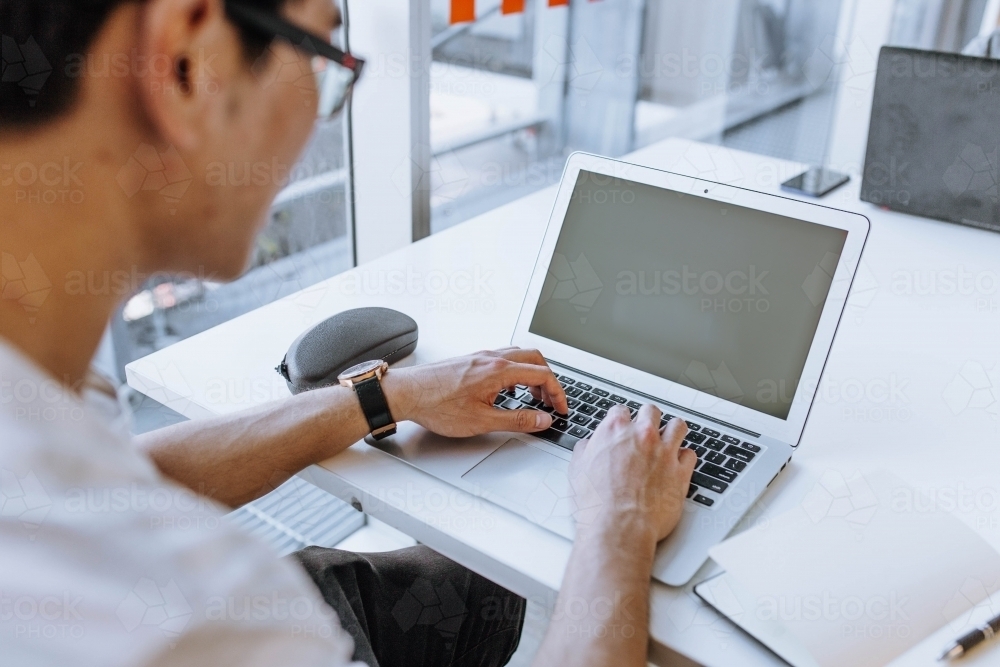 Man wearing glasses typing on computer at library desk - Australian Stock Image