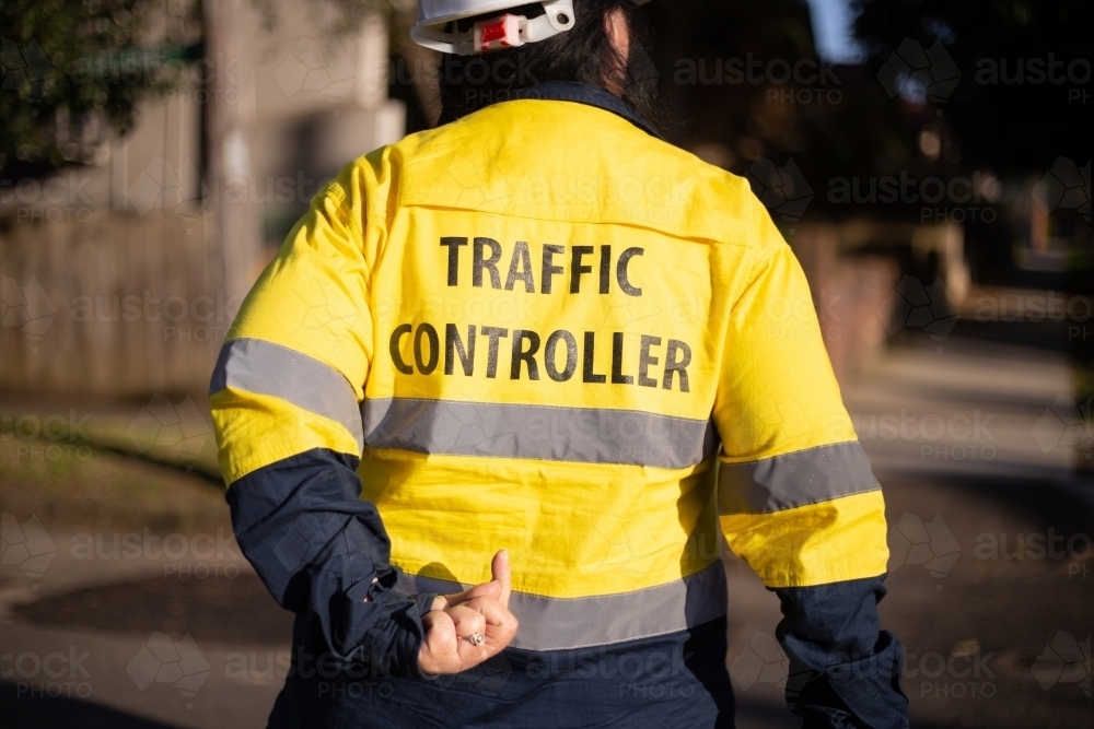 Back shot of a traffic controller wearing yellow jacket with silver reflectors - Australian Stock Image