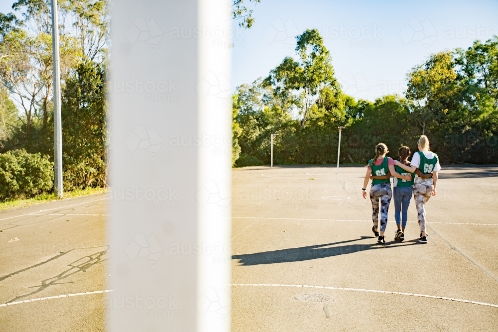 back shot of three young female athletes walking in a field on a sunny day with trees and clear sky - Australian Stock Image