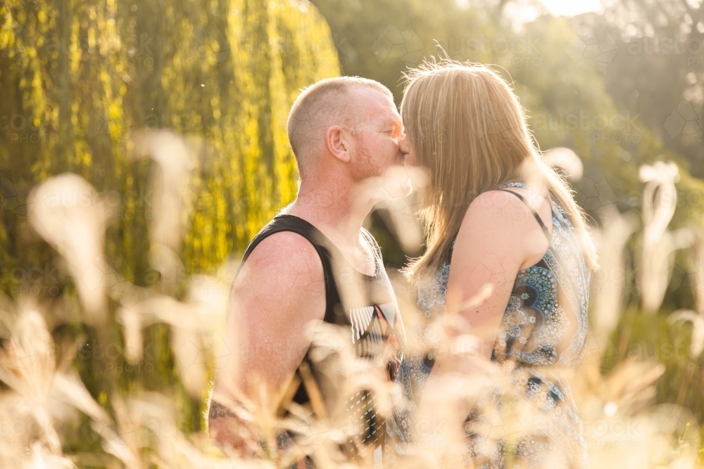 Backlit couple standing close together hidden behind grass - Australian Stock Image