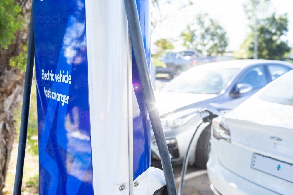 Backlit ev charger plugged into electric car in public parking lot - Australian Stock Image