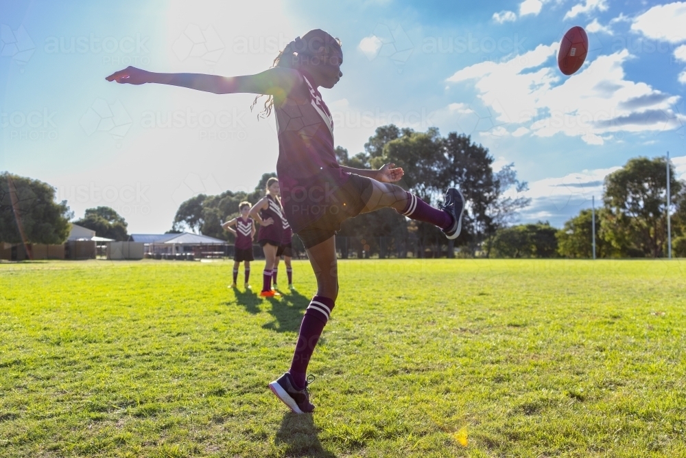 backlit with sunflare kid kicking aussie rules football - Australian Stock Image