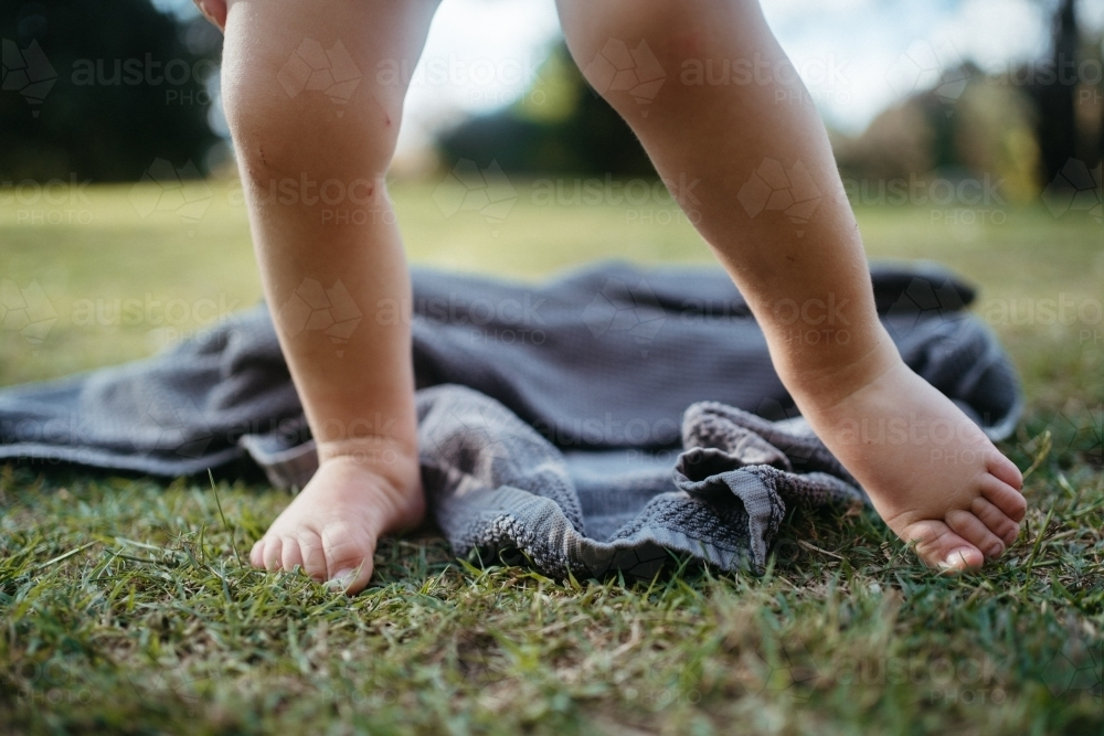 Bare toes of a toddler on the grass with a dropped towel - Australian Stock Image