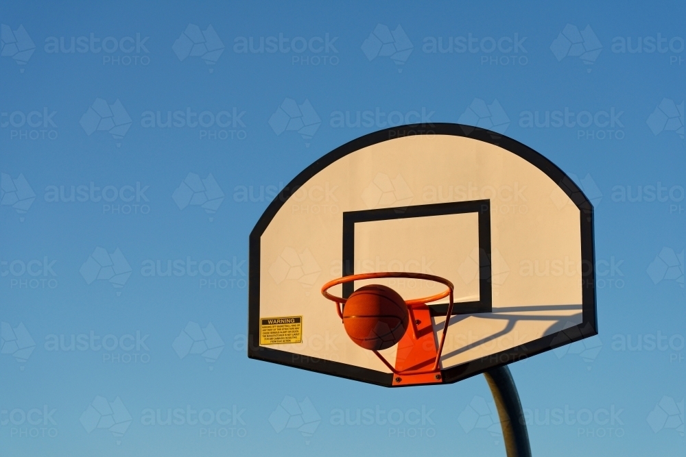 Basketball hoop and ball against a blue sky at sunset at a park - Australian Stock Image