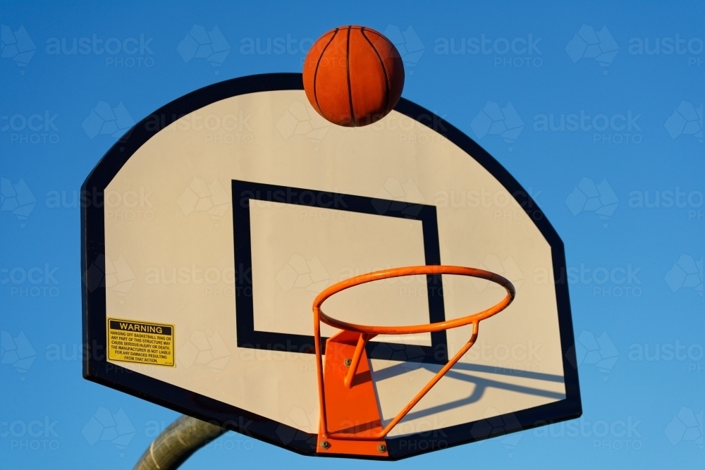 Basketball hoop and ball against a blue sky at sunset at a park - Australian Stock Image