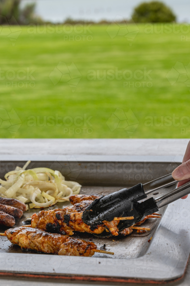 BBQ tray with grilled chicken, sausages, and caramelized onions cooking on it in park - Australian Stock Image