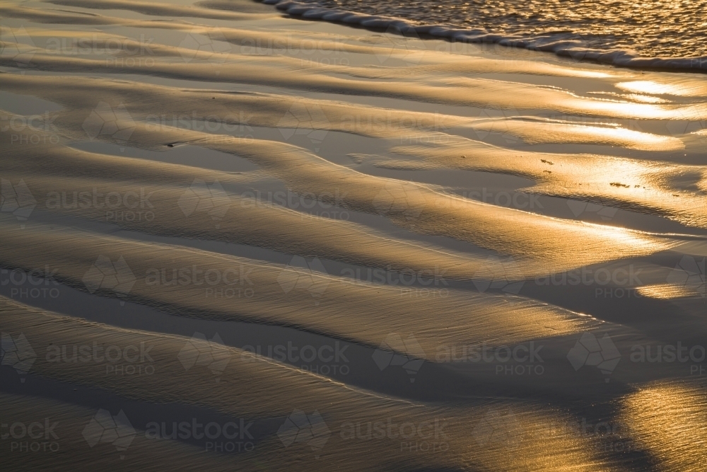 Beach ripple pattern of sand and water in golden light - Australian Stock Image