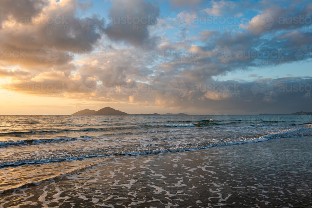 Beach scene at sunrise with waves and island - Australian Stock Image