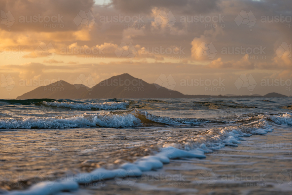 Beach scene at sunrise with waves and island - Australian Stock Image