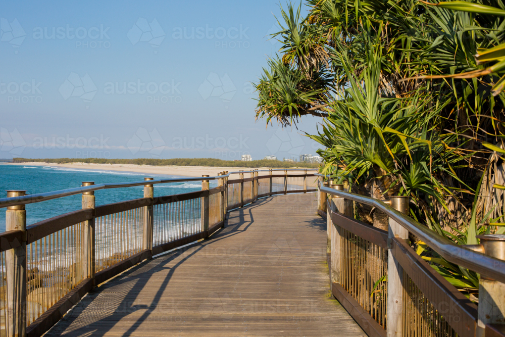 Beachside boardwalk curves along tropical coast. Empty path offers peaceful ocean views - Australian Stock Image