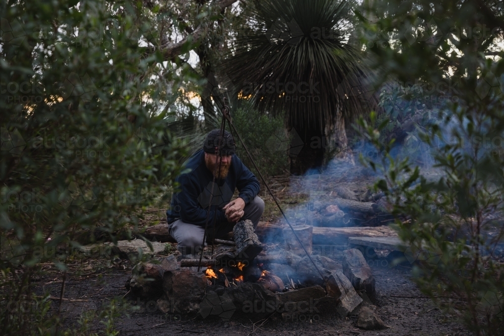 Bearded man tending to camp fire - Australian Stock Image