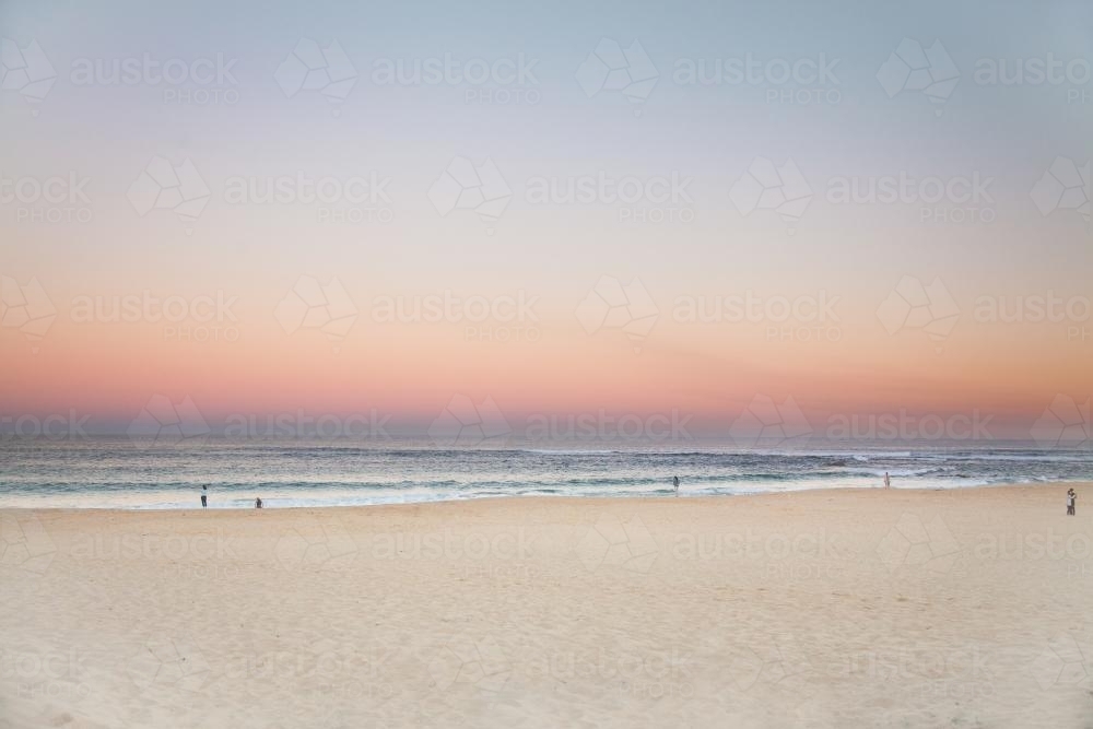 Beautiful sunset over a sandy beach with people in the distance - Australian Stock Image