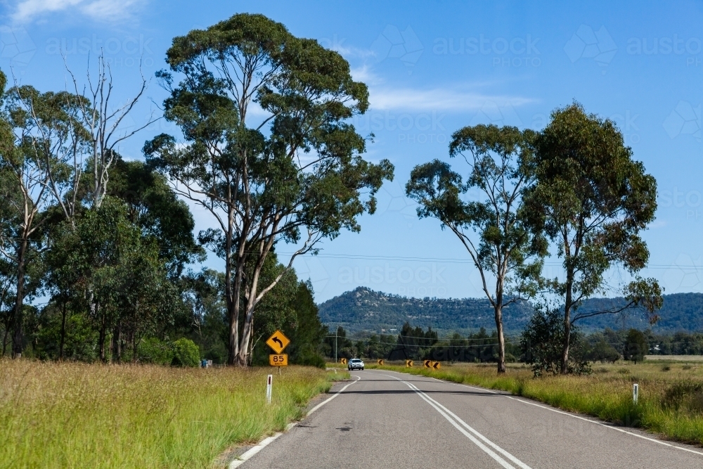 Bend in road ahead slow down sign beside highway - Australian Stock Image