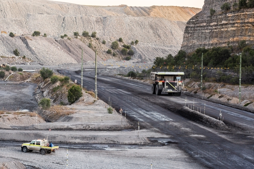 big mining operation truck and small vehicle driving on gravel road in open cut mine - Australian Stock Image