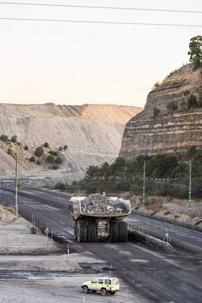 big mining operation truck and small vehicle driving on gravel road in open cut mine - Australian Stock Image