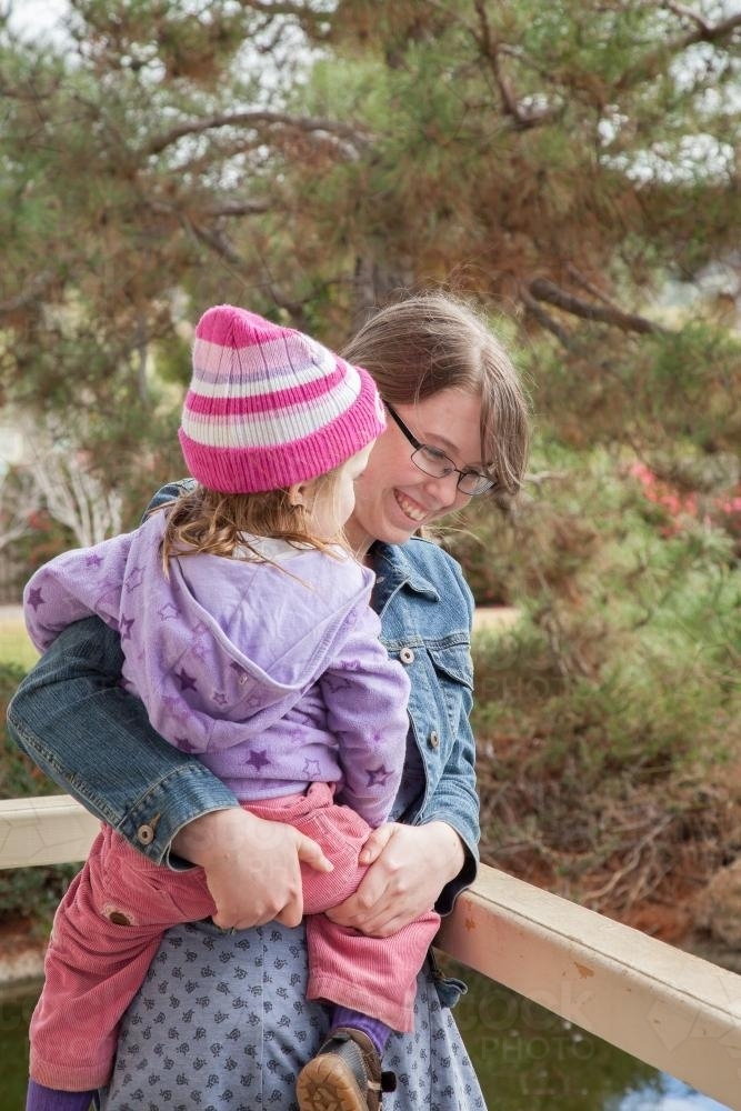 Big sister holding little sister and laughing together beside pond - Australian Stock Image