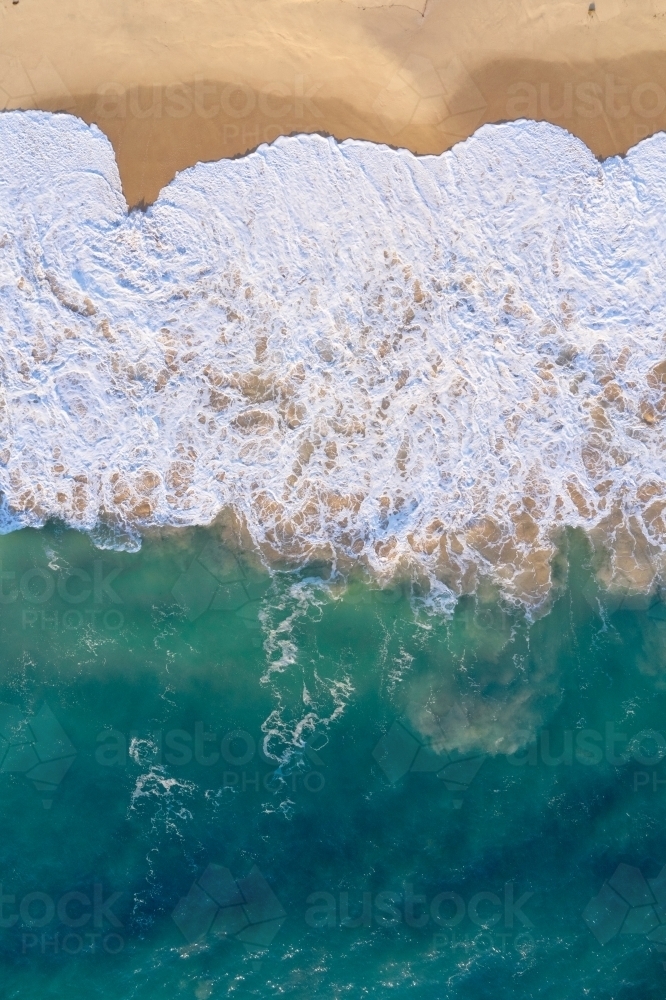 Bird's eye view of a wave washing ashore with lots of froth on a Western Australian beach. - Australian Stock Image