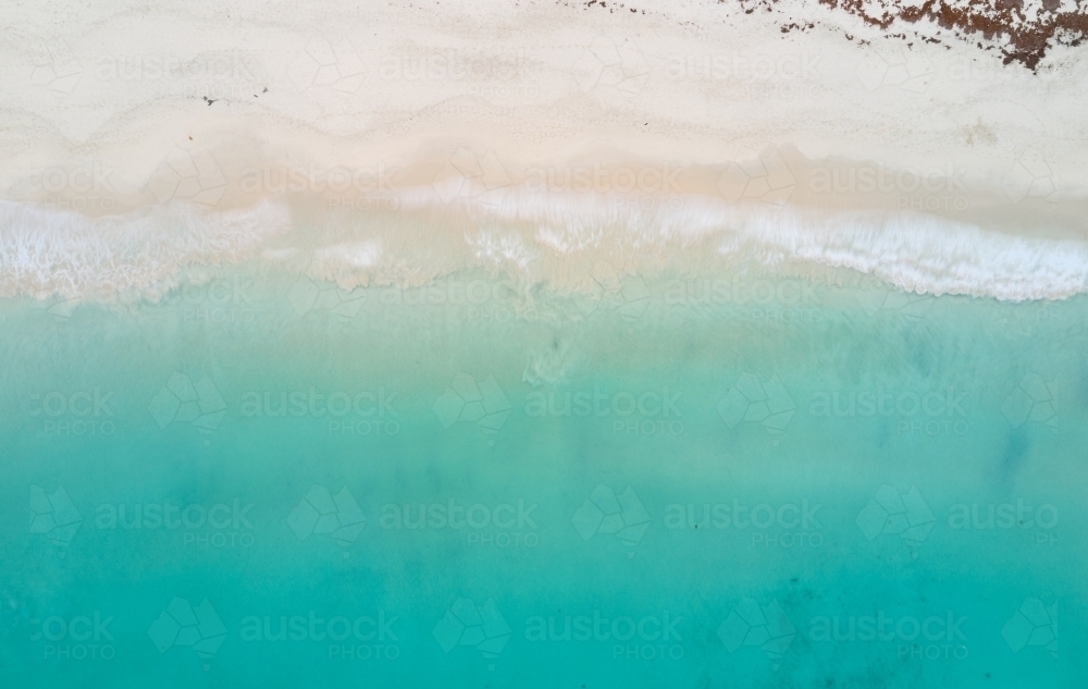Bird's eye view of turquoise ocean waters lapping onto a sandy beach - Australian Stock Image