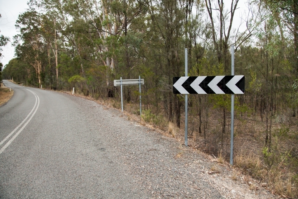 Black and white sign warning of sharp corner bend in country road - Australian Stock Image